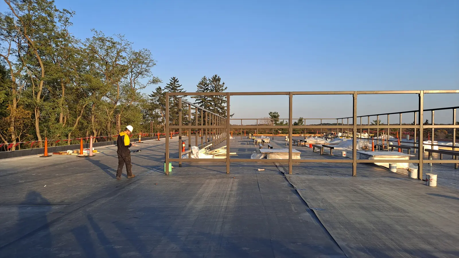 Roofer walking large commercial flat roof with steel framing at golden hour, EPDM membrane installed, Metro Detroit