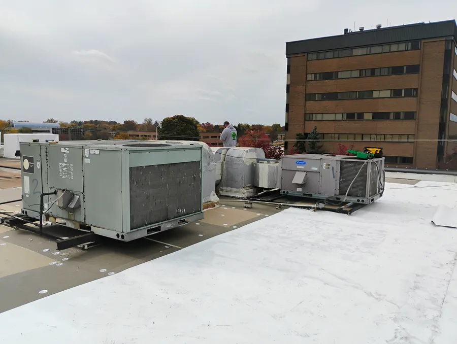 Roofing crew working around HVAC units on a commercial flat roof in Metro Detroit