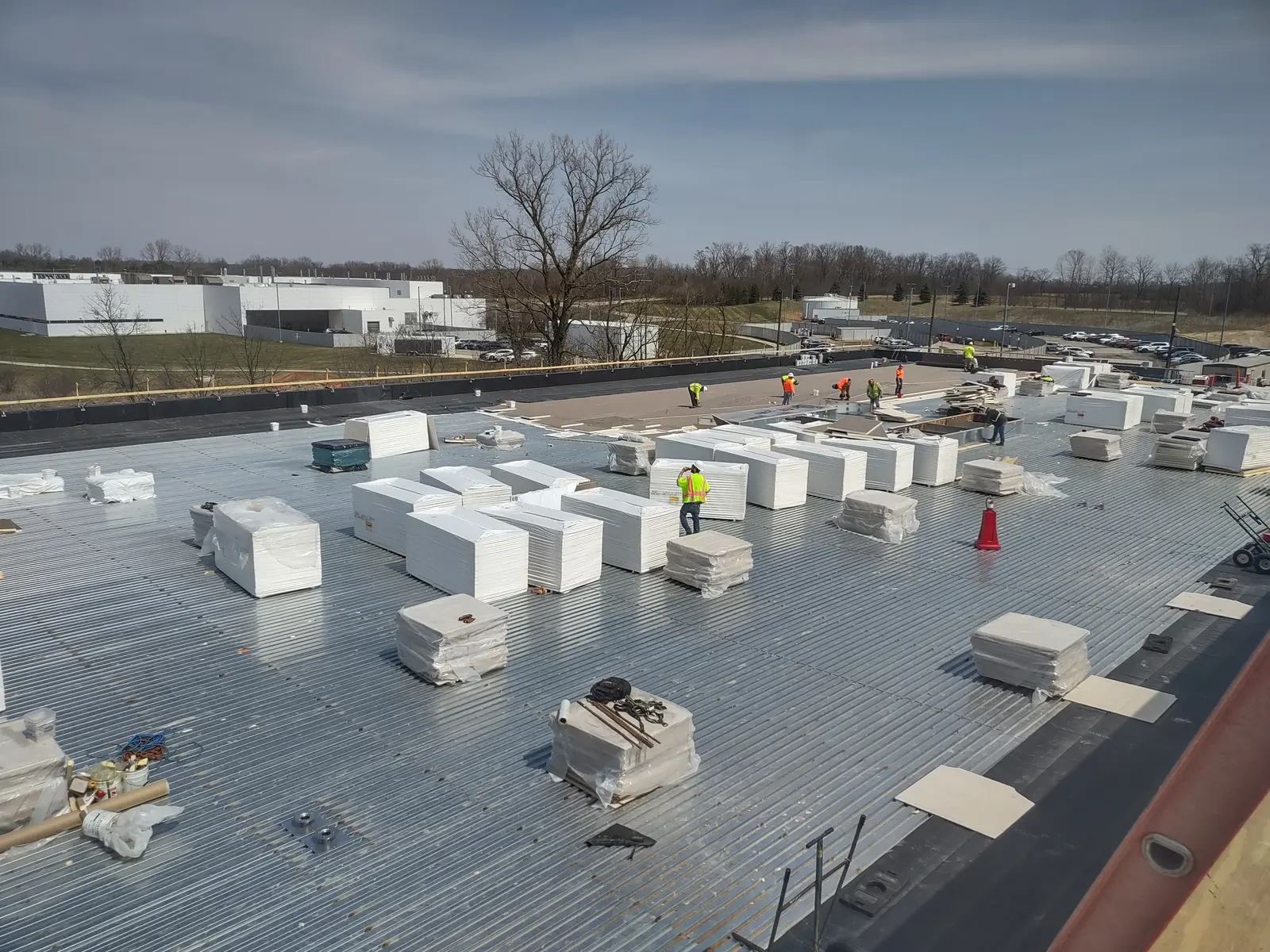 Stacks of insulation boards across large commercial flat roof with crew members working in background, Metro Detroit